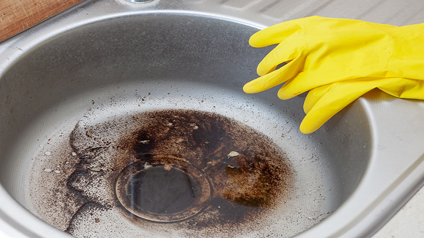 Yellow cleaning cloves sitting on the edge of a blocked sink