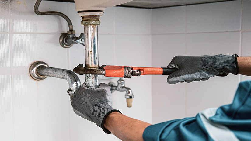 man holding a tool to fix a pipe under a sink